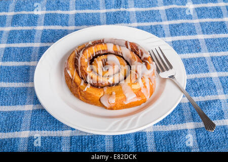 A fresh cinnamon roll on a white plate with fork Stock Photo