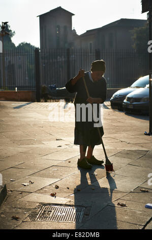 Old woman sweeping the sidewalk in the morning sun in Rome, Italy Stock Photo