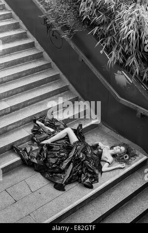 Woman wearing dress made from bin bags lying on stairs Stock Photo