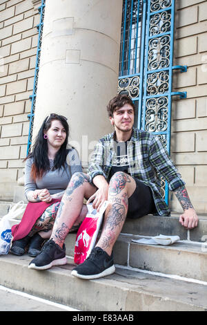 A young couple with tattoos sit on steps at City Hall in Sheffield City Centre UK Stock Photo