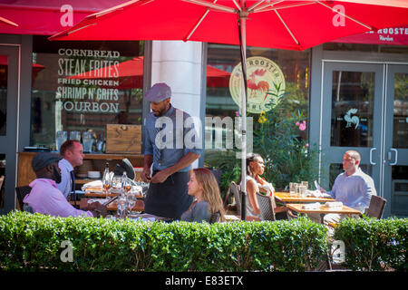 Patrons are served at the outdoor cafe of the Red Rooster restaurant on Lenox Avenue in the neighborhood of Harlem Stock Photo