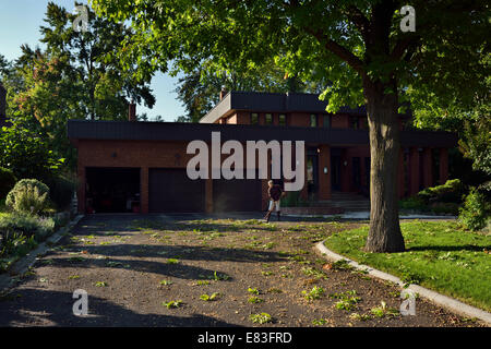 Woman homeowner sweeping mass of acorns for large Oak tree off a large three car garage circular driveway Stock Photo