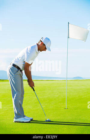 Golfer on Putting Green Hitting Golf Ball into the Hole Stock Photo