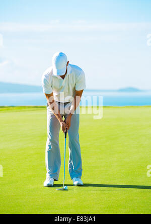 Golfer on Putting Green Hitting Golf Ball into the Hole Stock Photo