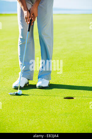 Golfer on Putting Green Hitting Golf Ball into the Hole Stock Photo