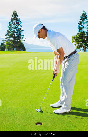 Golfer on Putting Green Hitting Golf Ball into the Hole Stock Photo