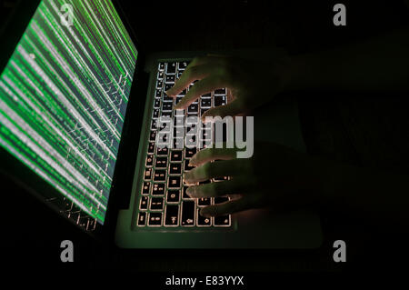 Computer hacker typing on keyboard with green matrix style graphics on the monitor Stock Photo