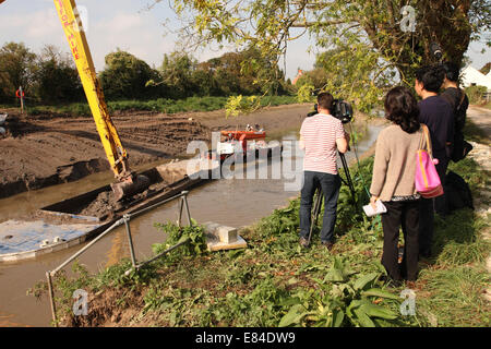 Burrowbridge, Somerset, UK. 30th September, 2014.  An international media TV crew watch as the dredging continues along the River Parrett on the Somerset Levels. Today river silt from mid channel of the Parrett is transferred by barge before offloading onto tractor & trailers for spreading on local fields. Stock Photo