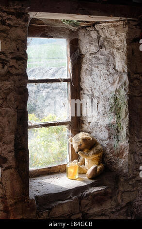 Threadbare One Eyed Teddy bear on an old window ledge looking at a pot of honey Stock Photo