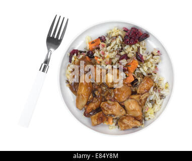 Top view of a cooked TV dinner with chicken in a pecan sauce, rice and cranberries in a small plate with fork to the side. Stock Photo