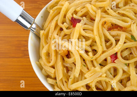 Close view of a serving of Chow Mein noodles with shrimp and seasonings in a small bowl with a spoon on a wood table top. Stock Photo