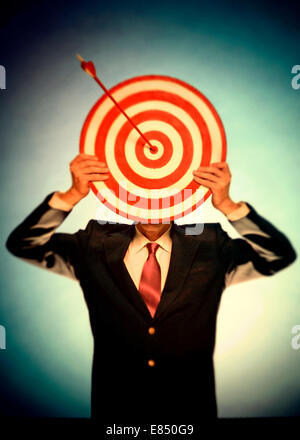 Businessman holding bullseye with arrow in front of his face Stock Photo