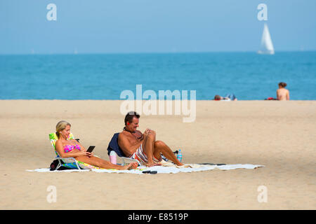 Couple on Beach, Oak Street Beach, Chicago Using Mobile Devices Stock Photo