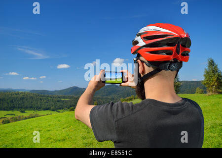 Cyclist taking picture with smart phone. Caucasian man in bike helmet taking photo of landscape. Outdoor activity. Copy space. Stock Photo