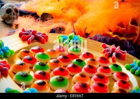 a pile of different Halloween candies with scary ornaments in the background, such as skulls, spiders and pumpkins Stock Photo