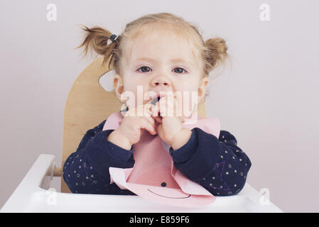 Baby girl sitting in high chair, eating snack Stock Photo