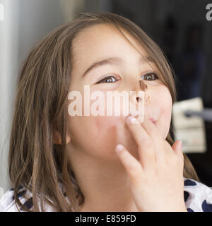 Girl with chocolate smeared on her nose, licking fingers Stock Photo