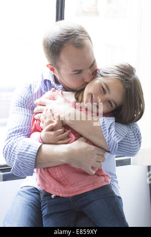 Father holding daughter on his lap, kissing her cheek Stock Photo