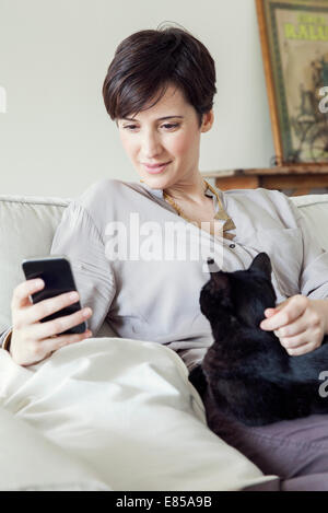 Woman sitting on sofa with cat on her lap, using smartphone Stock Photo