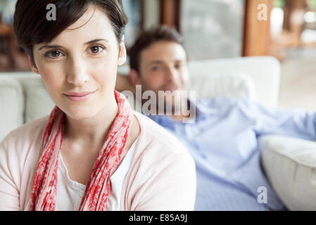 Woman sitting in living room with husband in background, portrait Stock Photo