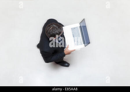 Businessman standing in lobby, using laptop computer Stock Photo