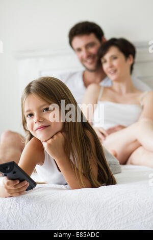 Little girl watching tv in bedroom with parents Stock Photo