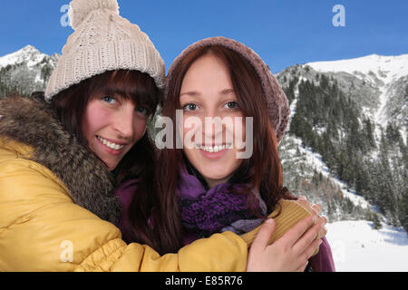 Two smiling women in winter clothing hug each other in the mountains Stock Photo