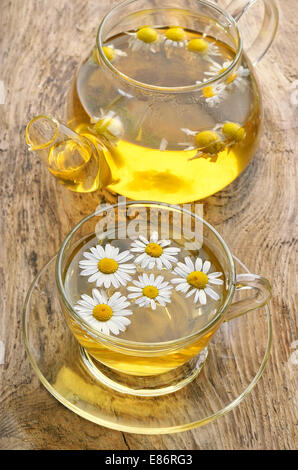 Chamomile tea in glass cup and tea pot on old wooden surface Stock Photo