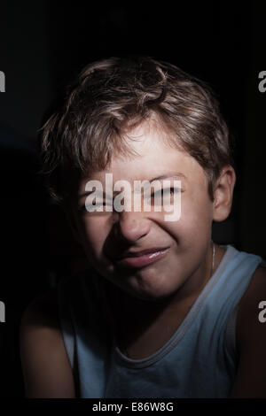 boy in the dark grimacing, focused light on the one side Stock Photo