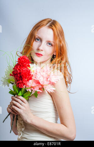 Cute 20s female with pretty flowers. Redhead women with bunch of flowers in studio on white. Blank expression. Stock Photo