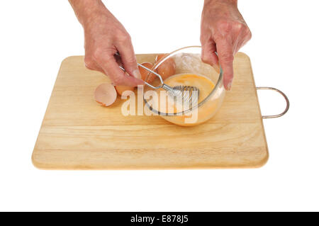 Closeup of hands beating eggs with a whisk in a glass bowl on a wooden board isolated against white Stock Photo