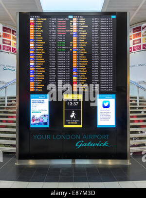 London Gatwick North Terminal gates info and flight departures board. Walking distances sign, clock, Twitter announcement. Stock Photo