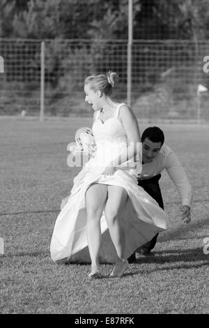 Trash the dress, bride and groom playing rugby, groom tackling the bride Stock Photo