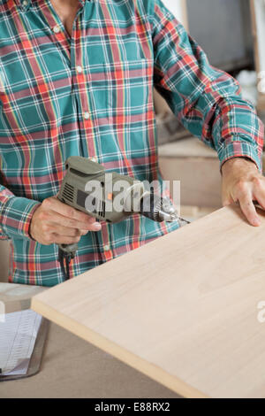Carpenter Using Electric Drill In Workshop Stock Photo