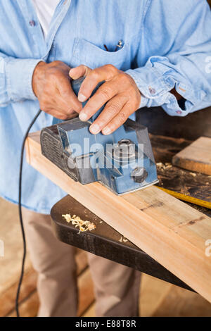 Senior Carpenter Shaving Wood With Electric Planer Stock Photo