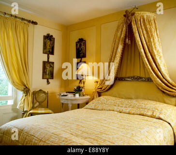 Coronet With Patterned Yellow Drapes Above Bed With Pale Yellow