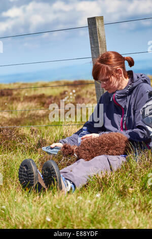 A female hiker feeding their dog while out on a walk in the countryside. Stock Photo