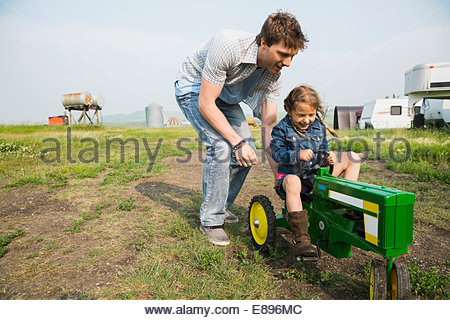Father pushing daughter on toy tractor in field