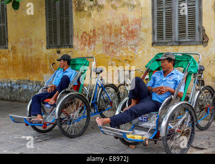 Two rickshaw drivers wait for customers while sitting in their rickshaws. Stock Photo