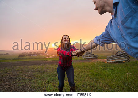 Woman pulling man in rural field at sunset