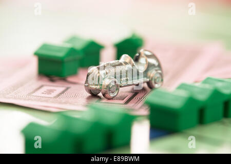 The Monopoly car game piece on yhe games' money with defocused houses on th board Stock Photo