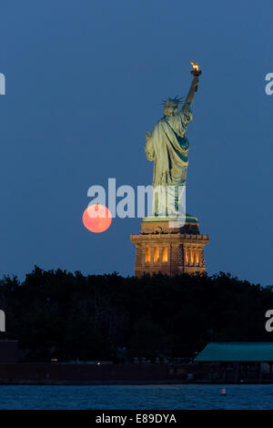 The super moon rises next to the Statue of Liberty during twilight. Stock Photo
