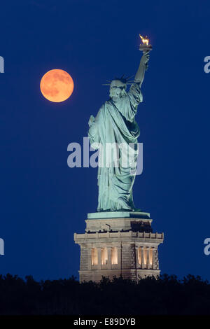 The super moon rises next to the Statue of Liberty during the blue hour. Stock Photo