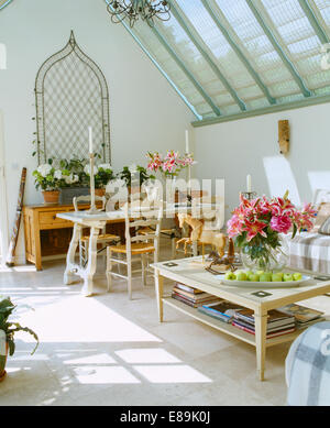 Vase of pink lilies on coffee-table in conservatory living and dining room with travertine floor and metal ogee trellis on wall Stock Photo