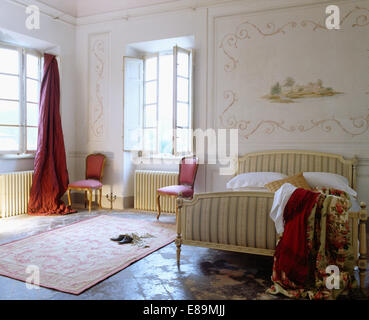 Richly patterned floral throw on striped upholstered bed in Tuscan bedroom with decoratively painted wall panel Stock Photo