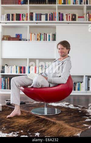 Portrait of mature man sitting on chair with book, smiling Stock Photo