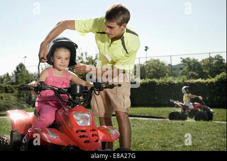 Tutor assisting girl with helmet on driver training area Stock Photo