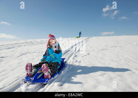 Girl sledging down hill, boy in background, Bavaria, Germany Stock Photo