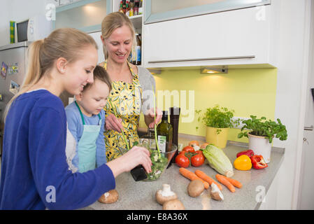 Mother and children preparing salad in kitchen, smiling Stock Photo