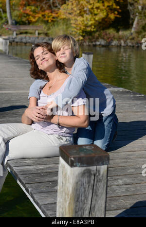 Mother and son sitting and embracing each other on boardwalk, Bavaria, Germany Stock Photo